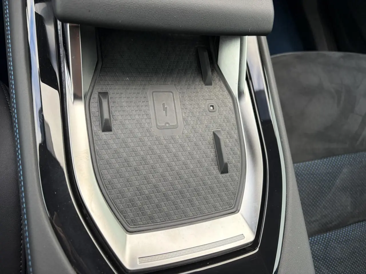 Gros plan sur la console centrale noire avec surface de recharge sans fil et surpiqûres bleues du siège Renault Rafale Summit Blue.