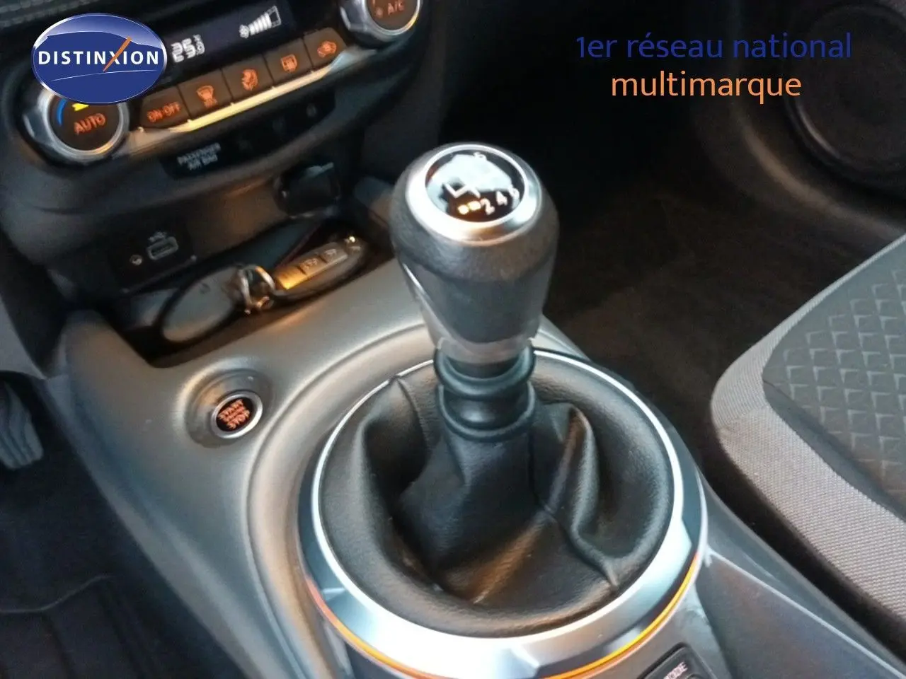 Gros plan sur le levier de vitesses manuel du Nissan Juke gris platine, avec console centrale et commandes climatiques visibles.