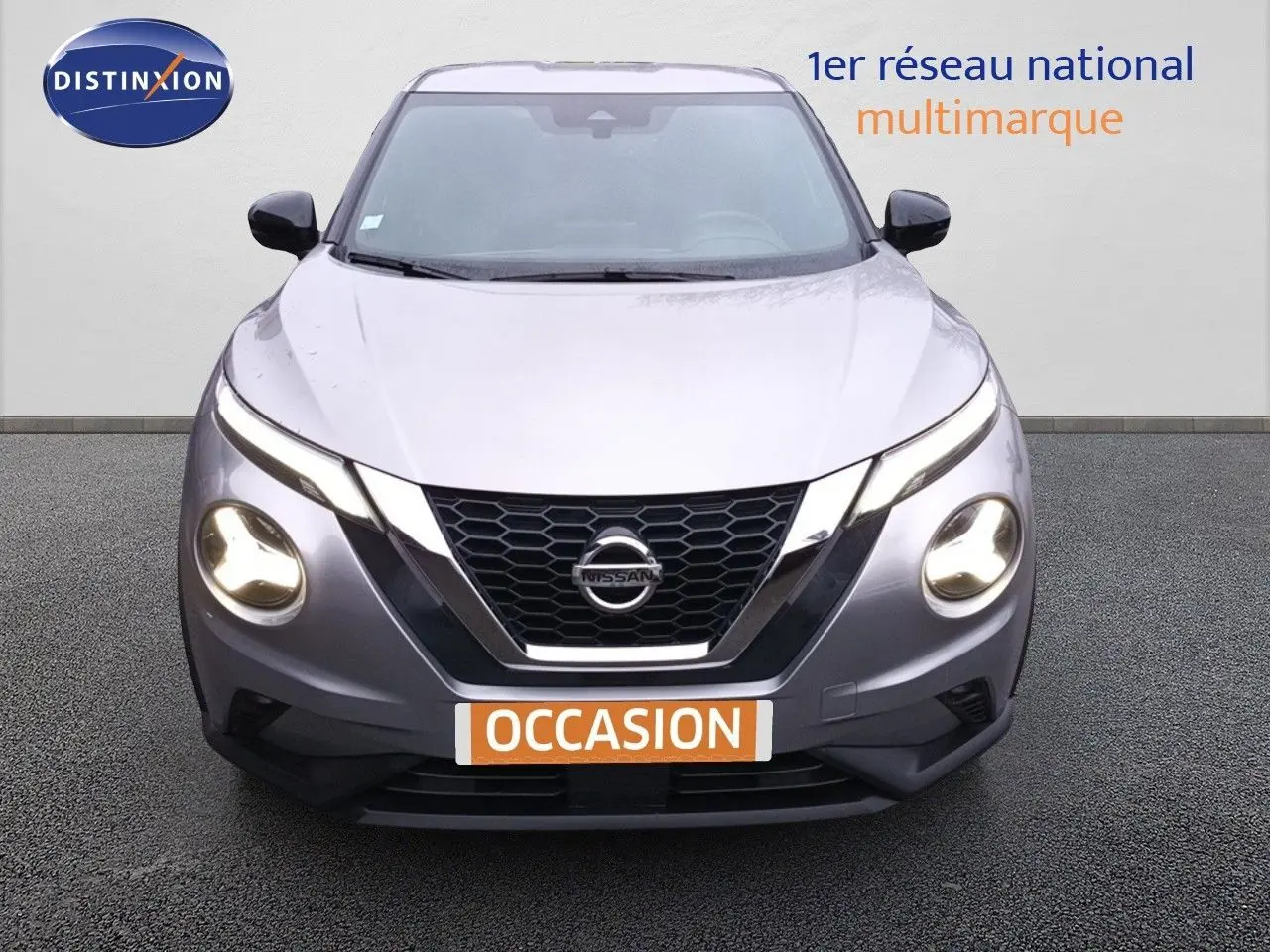 Vue frontale d'un Nissan Juke gris platine métal de 2020 avec phares allumés et calandre en nid d'abeille.