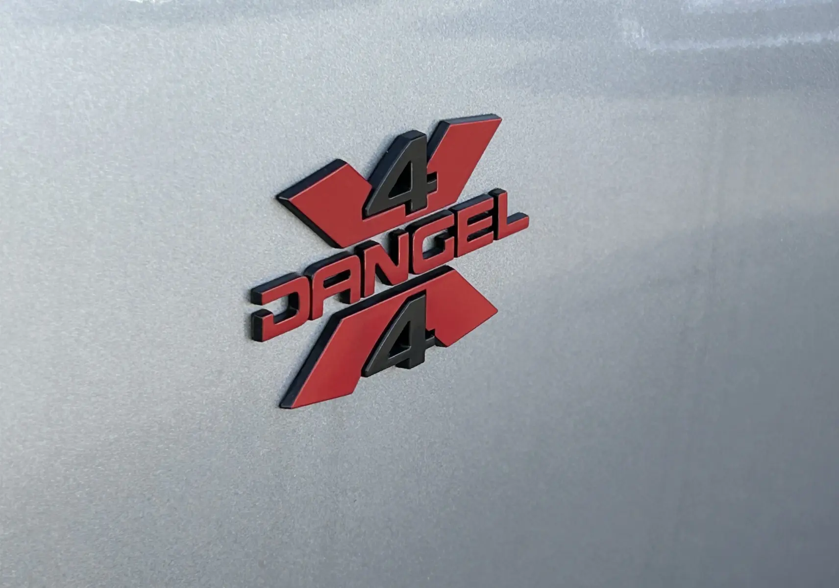 Gros plan sur le logo 4x4 Dangel rouge et noir apposé sur la carrosserie gris artense du Peugeot Partner.