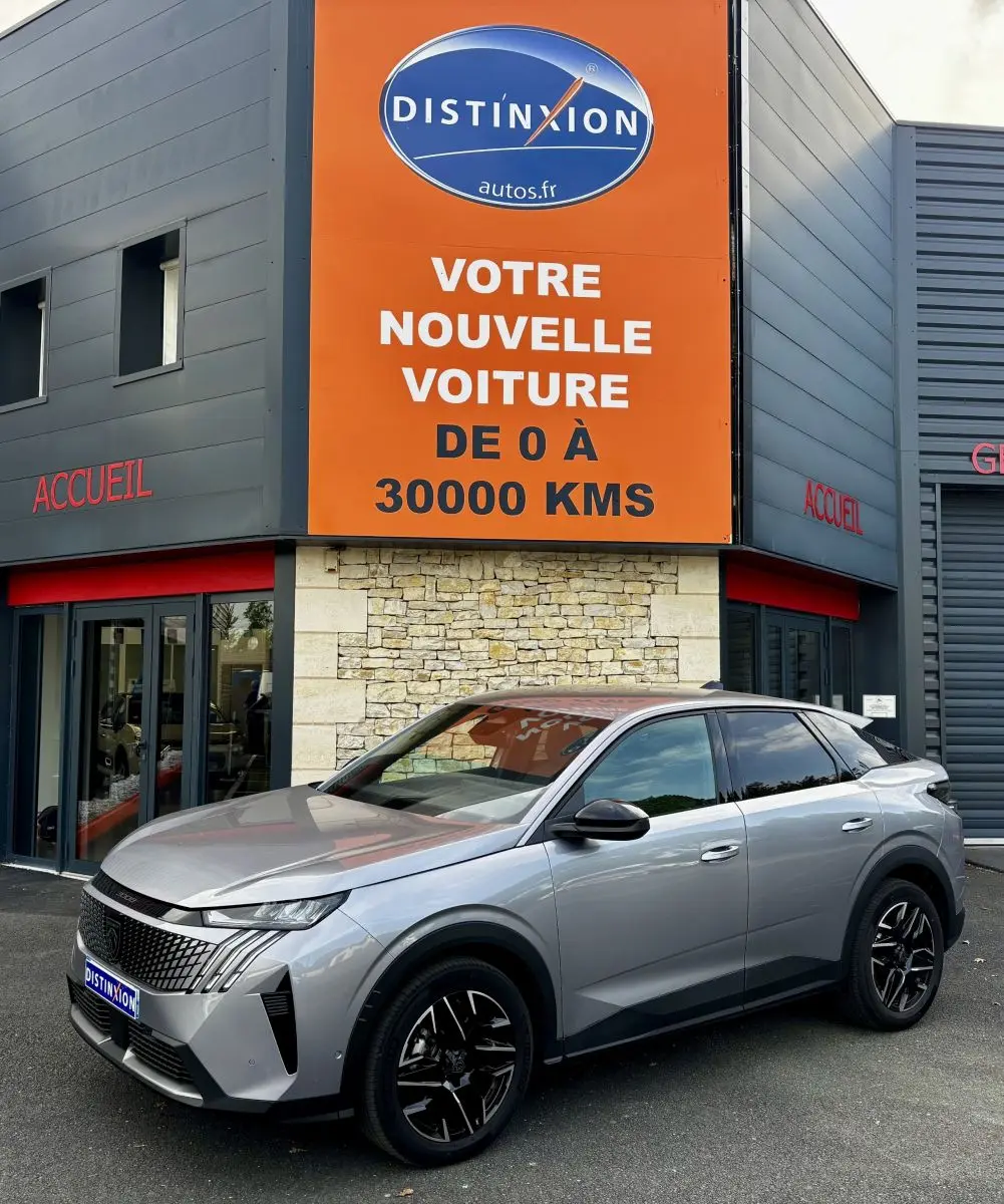 Peugeot 3008 gris clair vue 3/4 avant droit, avec calandre distinctive et jantes noires, devant un bâtiment commercial.