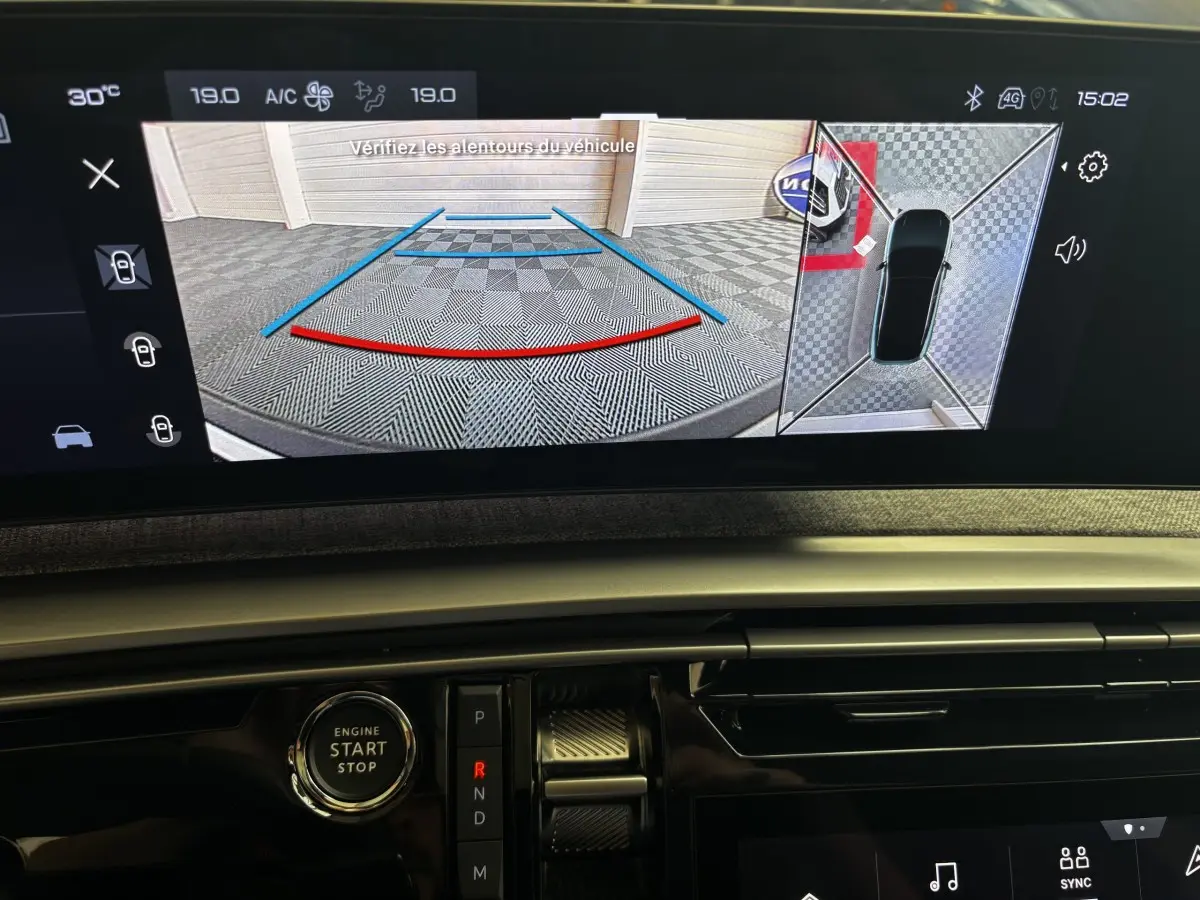 Vue intérieure du tableau de bord du Peugeot 3008 gris clair 2025, avec écran de caméra de recul et bouton démarrage visible.