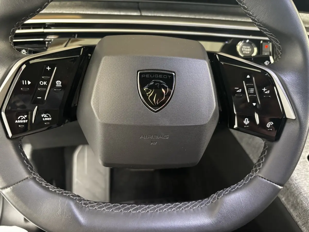 Gros plan sur le volant cuir noir du Peugeot 3008 2025 avec commandes multifonctions et bouton démarrage visible.