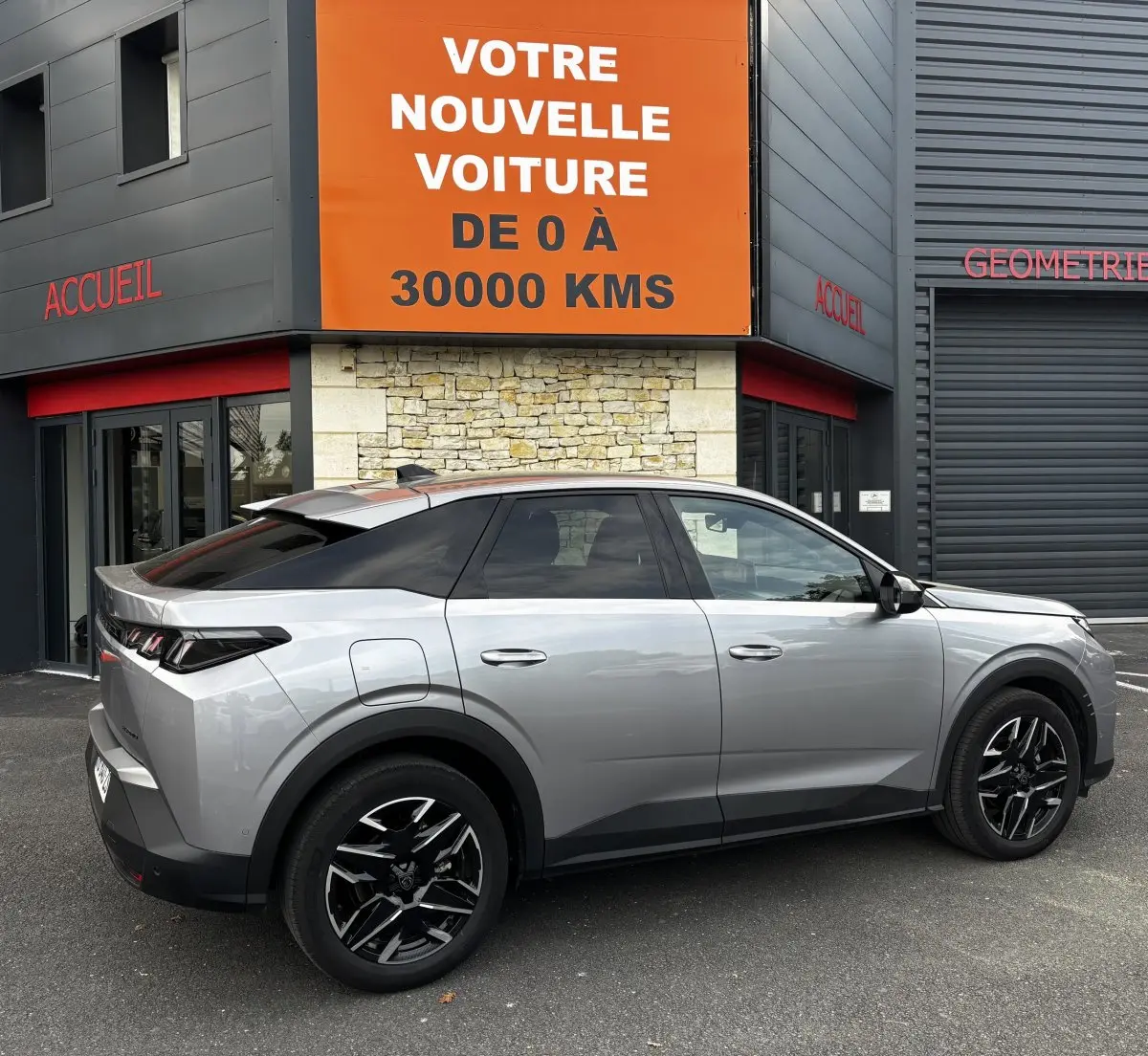 Peugeot 3008 gris clair vue de profil droit, avec jantes noires et toit noir contrastant, stationnée devant un bâtiment.
