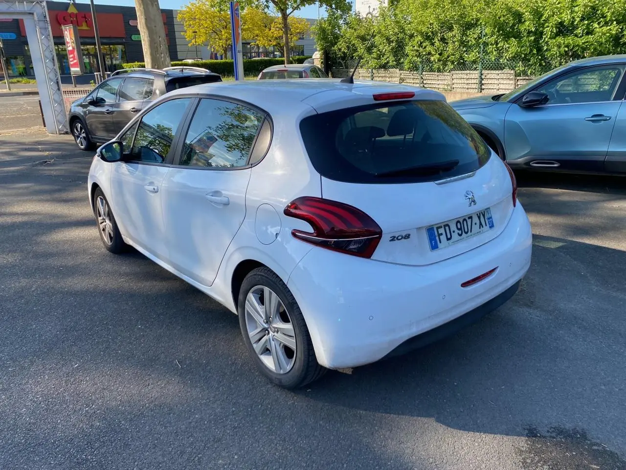 Peugeot 208 blanche vue en 3/4 arrière droit, avec feux arrière distinctifs et plaque d'immatriculation française.
