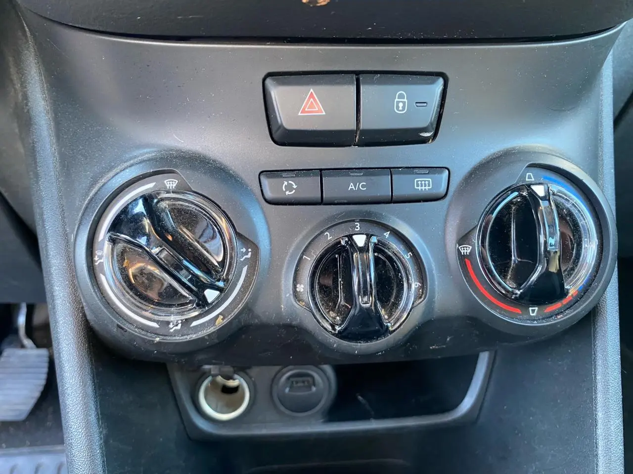 Gros plan sur les commandes de climatisation et boutons de sécurité du tableau de bord de la Peugeot 208 blanche 2019.