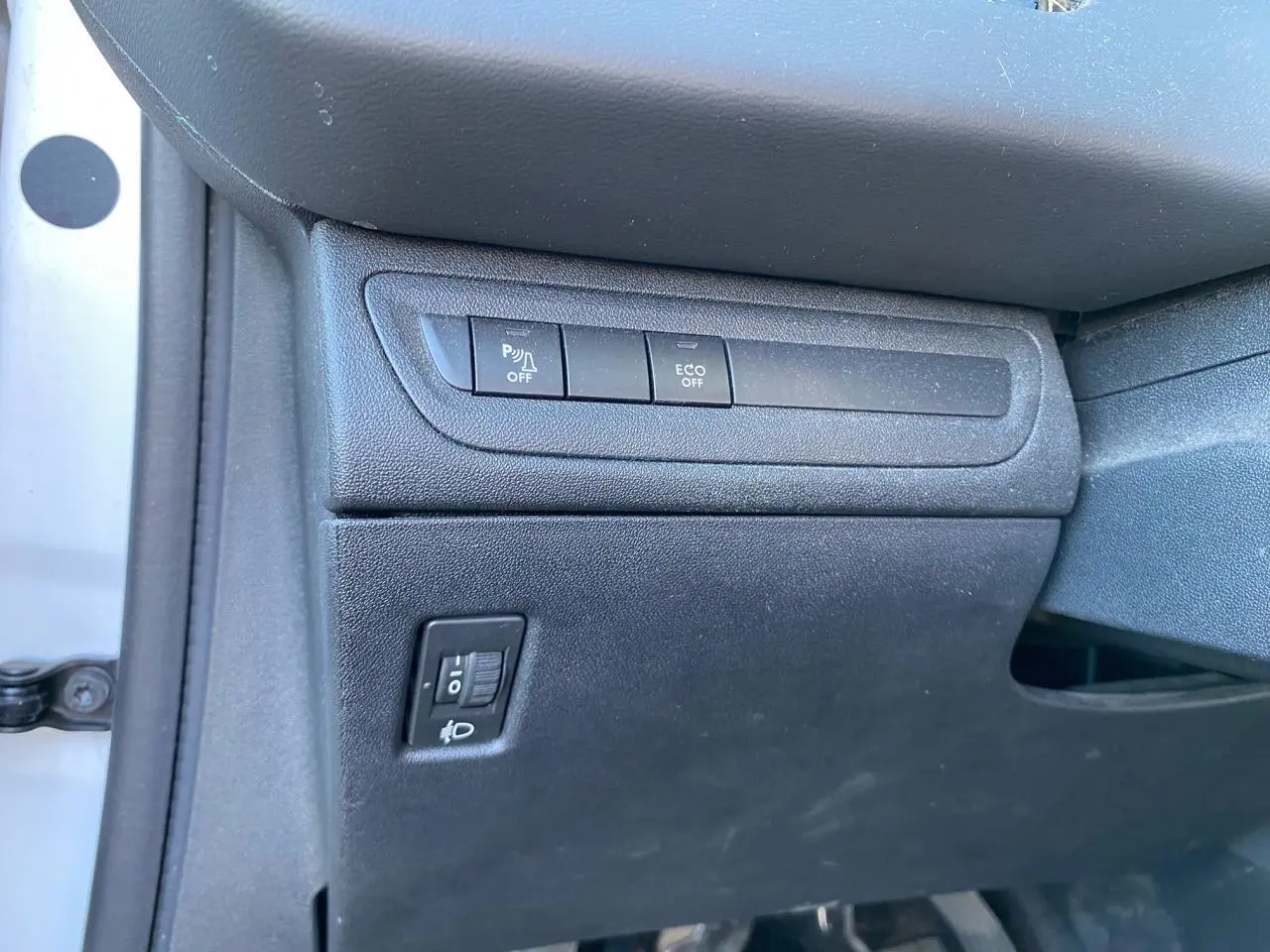 Détail intérieur côté conducteur du Peugeot 208 blanc 2019 montrant les commandes d’aide au stationnement et mode ECO.
