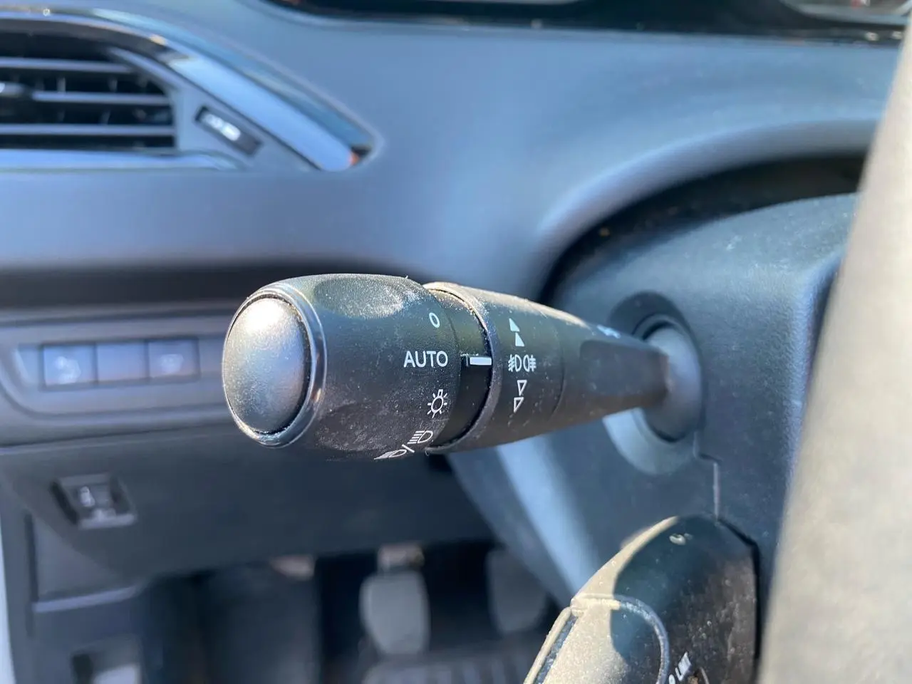 Gros plan sur la commande des feux à gauche du volant dans l’habitacle d’une Peugeot 208 blanche de 2019.