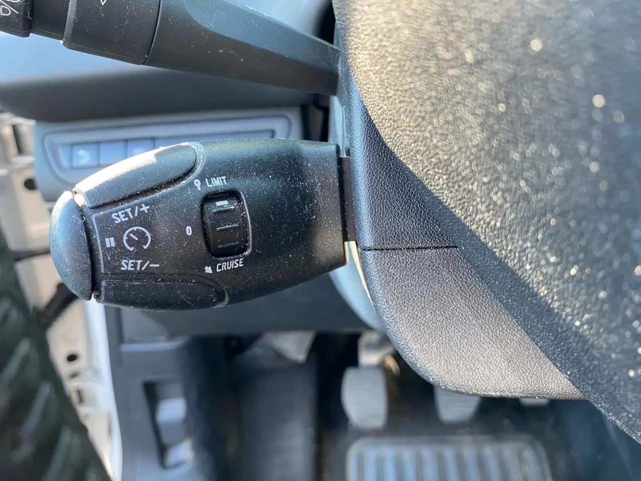 Gros plan sur la commande de régulateur de vitesse à gauche du volant dans une Peugeot 208 blanche de 2019.