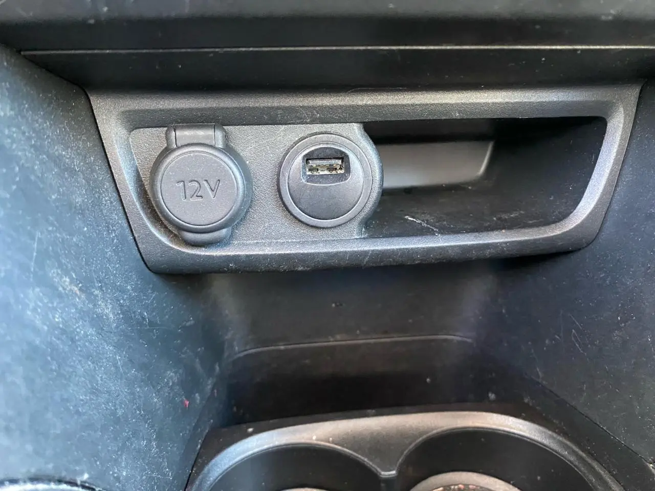 Gros plan sur la prise 12V et port USB dans l’espace de rangement intérieur noir d’une Peugeot 208 blanche.