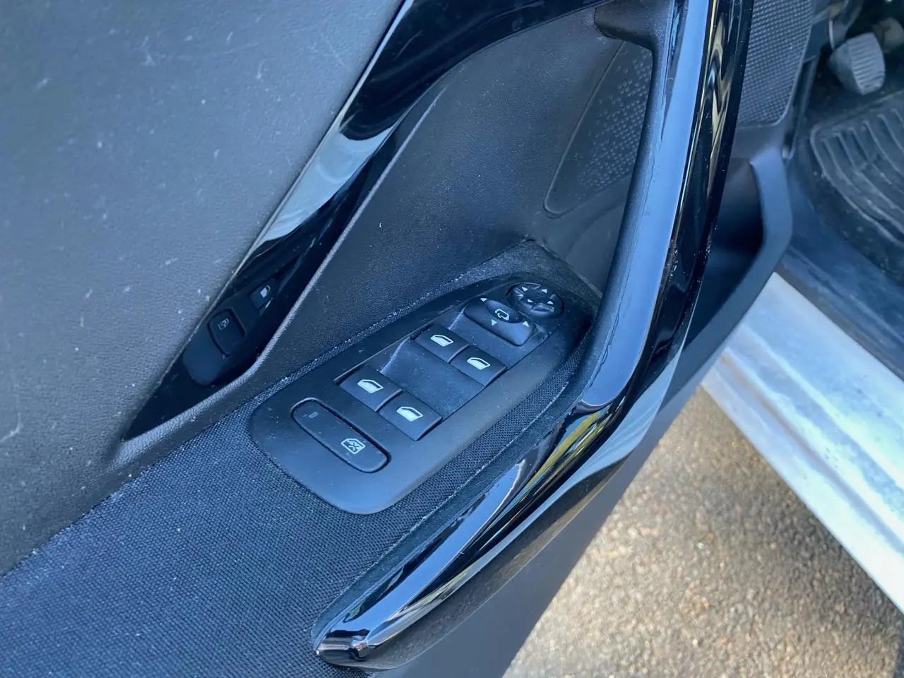 Gros plan sur les commandes des lève-vitres et réglages des rétroviseurs côté conducteur d'une Peugeot 208 noire.