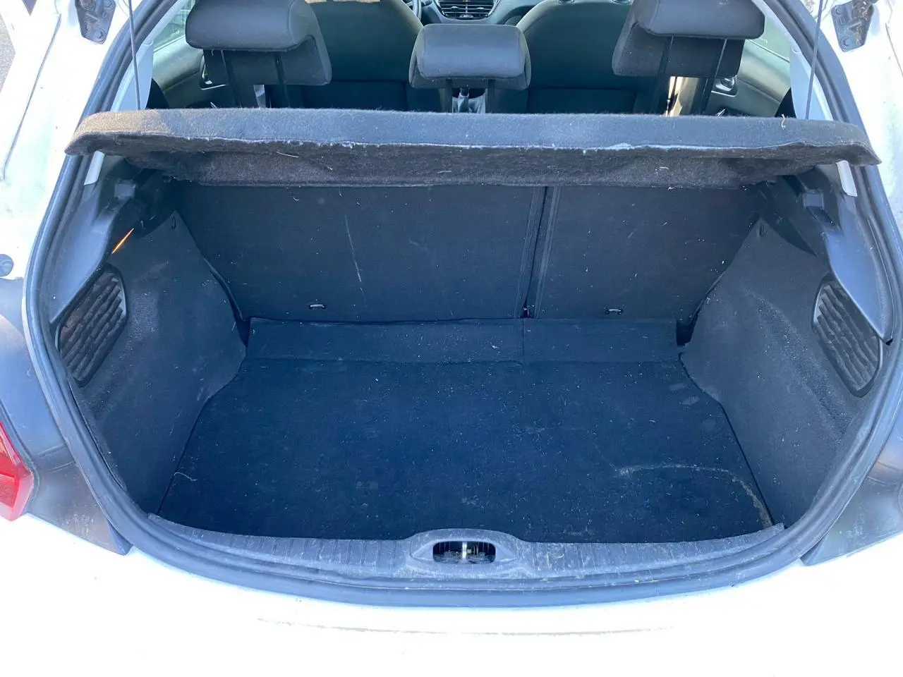Coffre ouvert vu de l'arrière d'une Peugeot 208 blanche, montrant l'espace de chargement et la banquette arrière.
