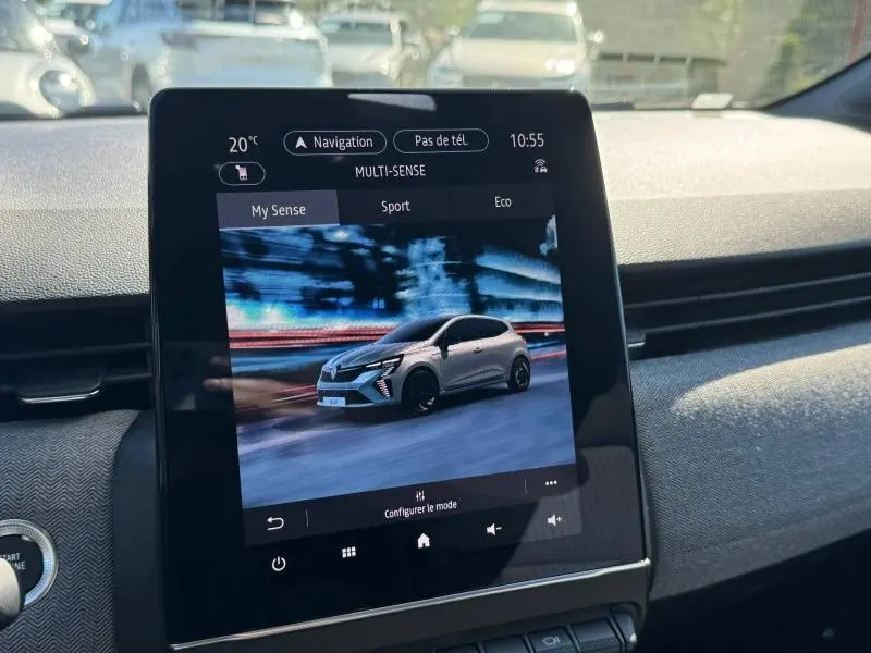 Écran tactile intérieur montrant une Renault Clio grise en mouvement, vue de profil dans un décor urbain nocturne.