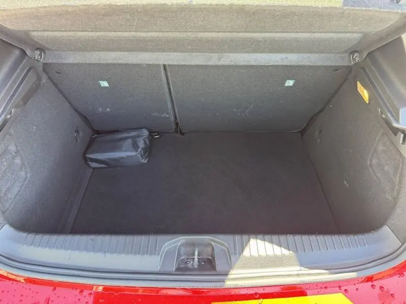 Coffre ouvert vu de dessus d'une Renault Clio rouge 2025, montrant un espace de rangement vide avec un sac noir.