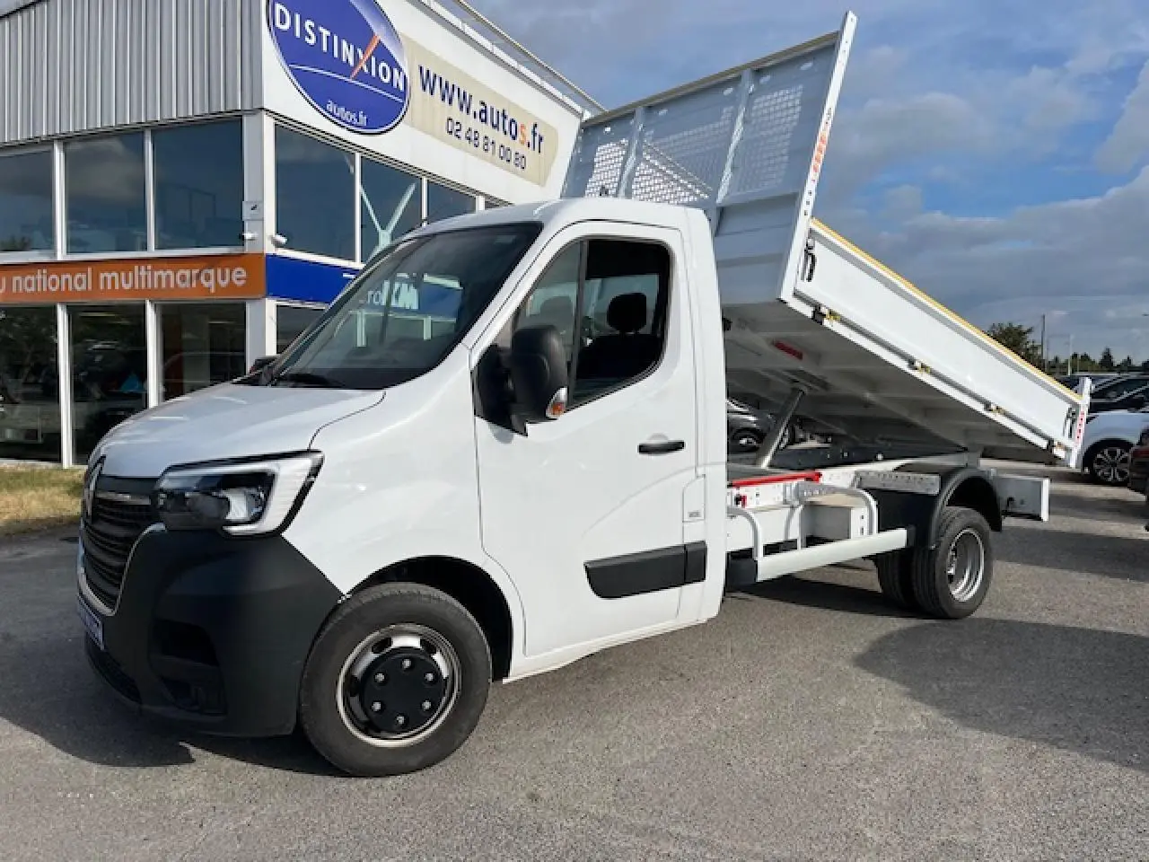 Renault Master blanc 2024 vue 3/4 avant droit avec benne basculante relevée sur parking extérieur.