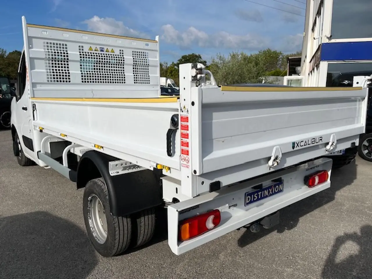 Vue 3/4 arrière droite du Renault Master blanc 2024 avec benne basculante et double roues arrière.