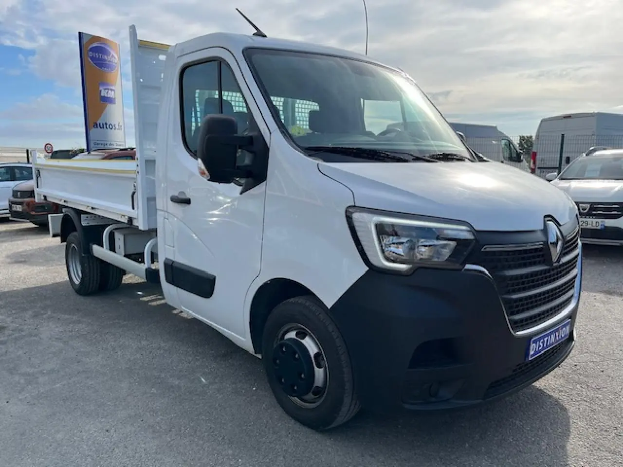 Renault Master blanc en 3/4 avant droit, benne basculante visible, calandre noire et pare-chocs avant noir.