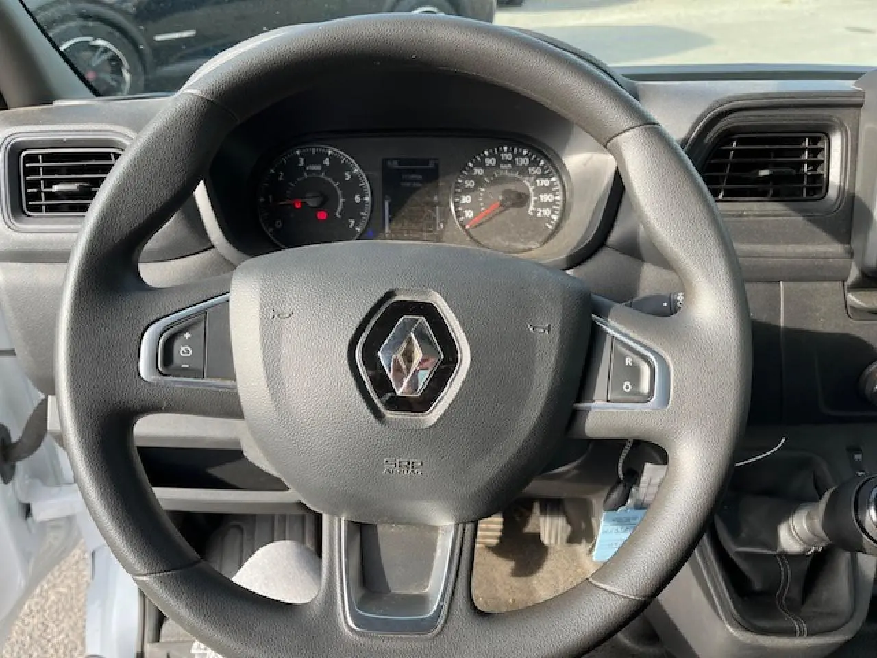 Vue rapprochée du volant noir avec logo Renault du Master 2.3 dCi 130 Benne Basculante blanc, tableau de bord en arrière-plan.
