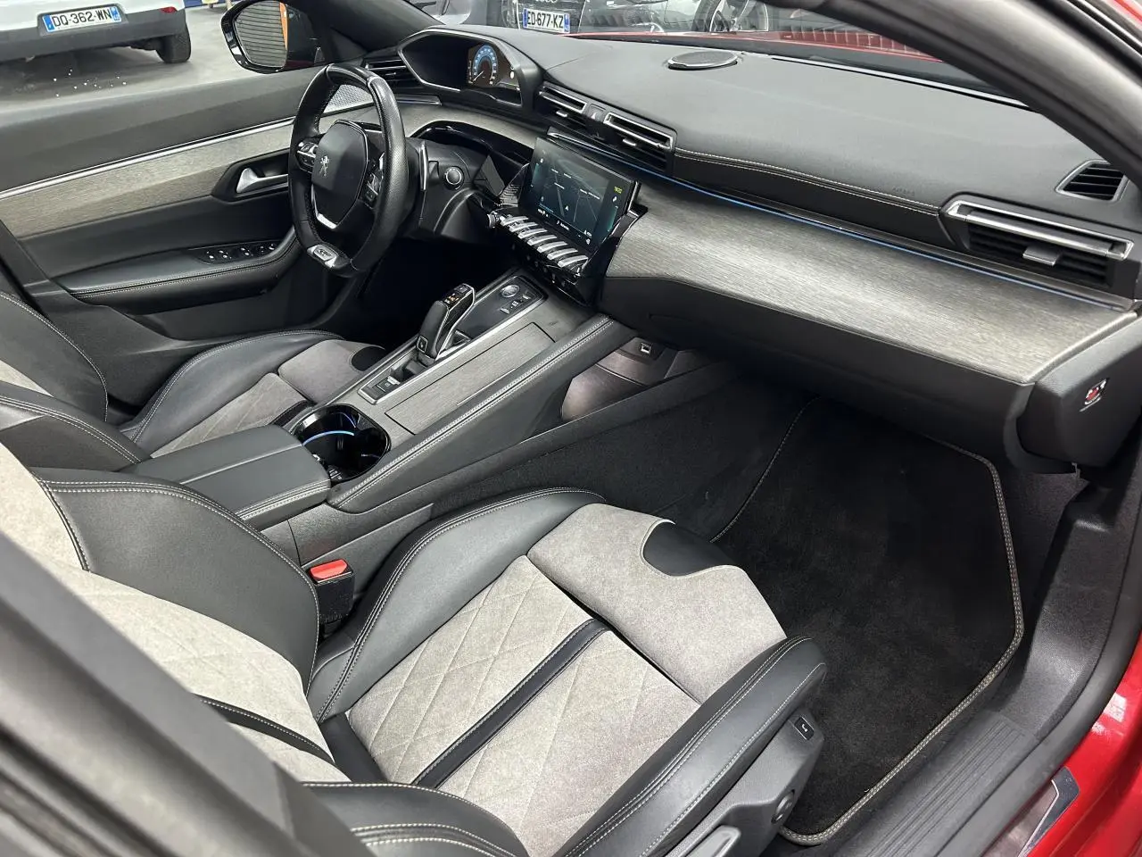 Intérieur avant droit de la Peugeot 508 Hybrid rouge clair, avec sellerie cuir et alcantara gris et tableau de bord moderne.