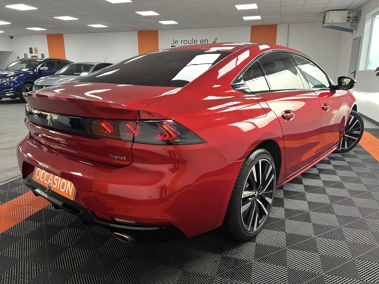Vue 3/4 arrière droite d'une Peugeot 508 rouge clair avec jantes alliage bi-ton et feux arrière LED distinctifs.