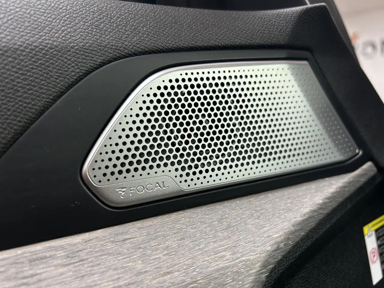 Gros plan sur l'enceinte Focal intégrée à la porte intérieure noire d'une Peugeot 508 Hybrid rouge clair.