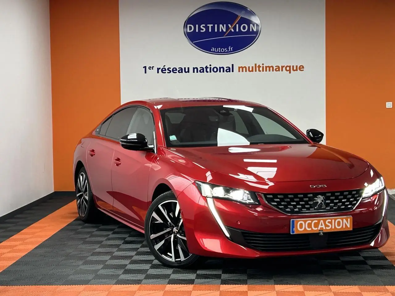 Peugeot 508 rouge clair vue 3/4 avant droit avec jantes alliage et feux LED allumés en showroom.