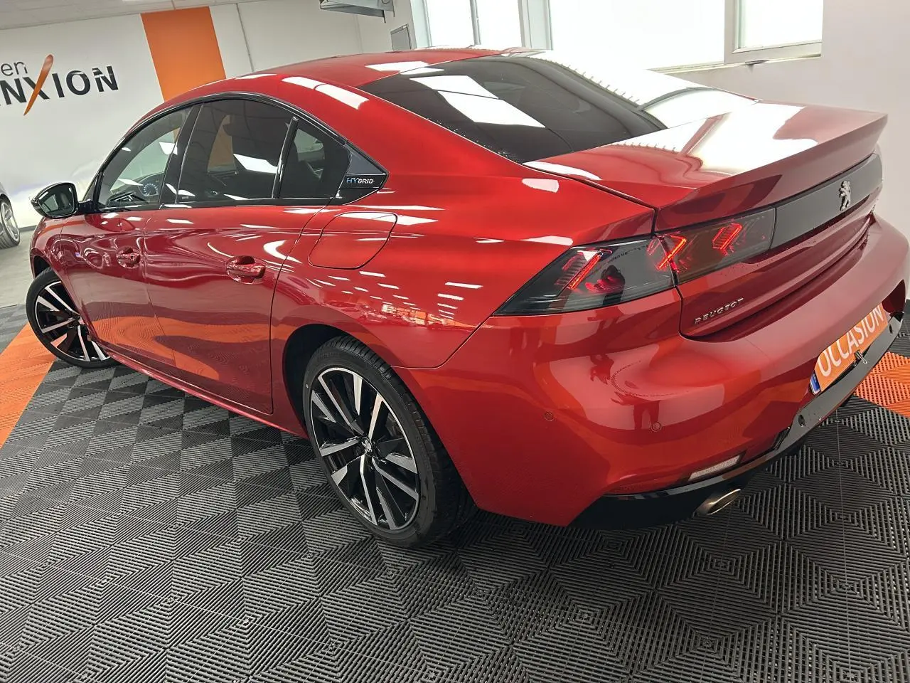 Vue 3/4 arrière droite d'une Peugeot 508 Hybrid rouge clair avec jantes alliage bi-ton et badge Hybrid visible.