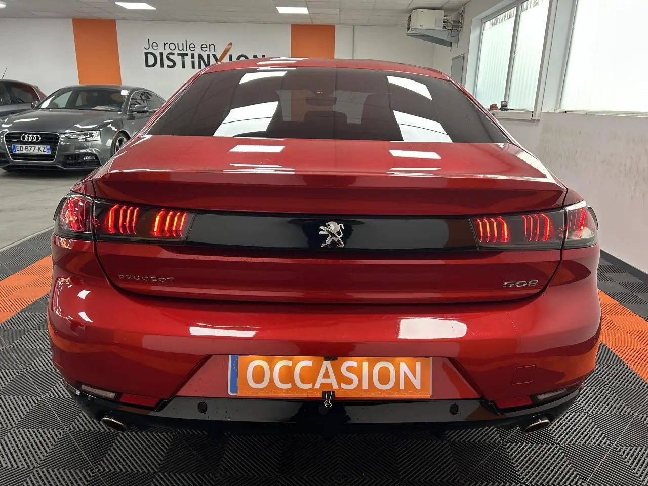 Vue arrière d'une Peugeot 508 rouge clair avec feux LED allumés dans un showroom.
