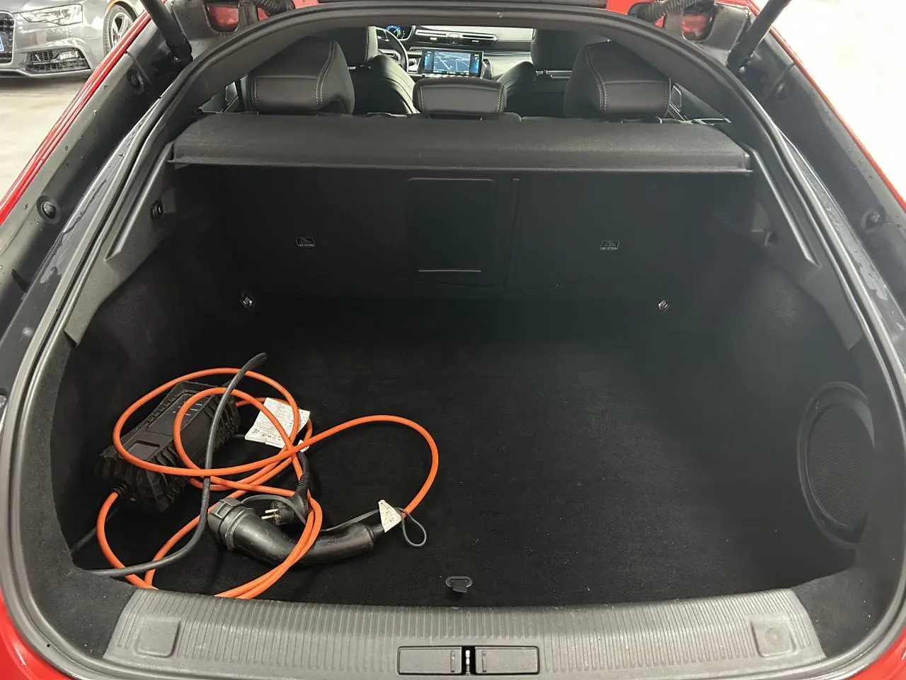 Coffre ouvert d’une Peugeot 508 Hybrid rouge clair avec câble de recharge électrique visible à l’intérieur.
