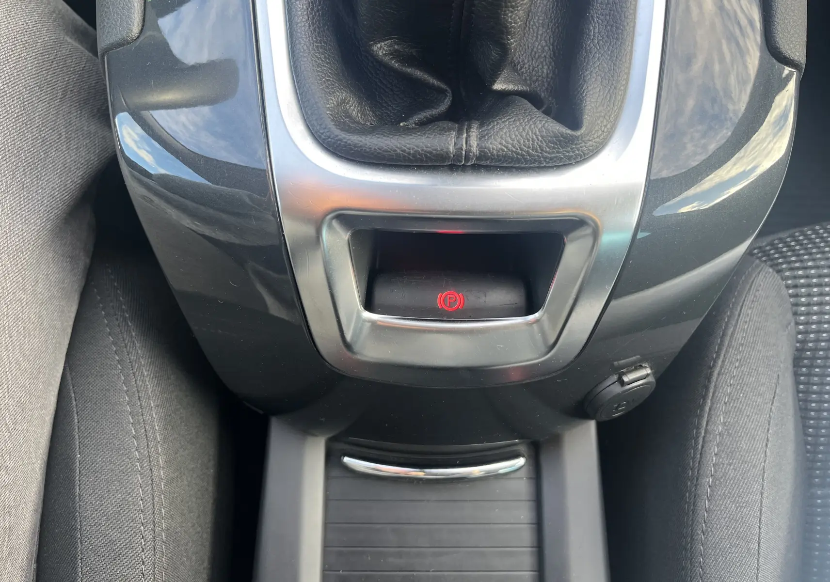 Gros plan sur la console centrale noire du Peugeot 5008 2013, mettant en valeur le frein à main électrique rouge et le levier de vitesse.