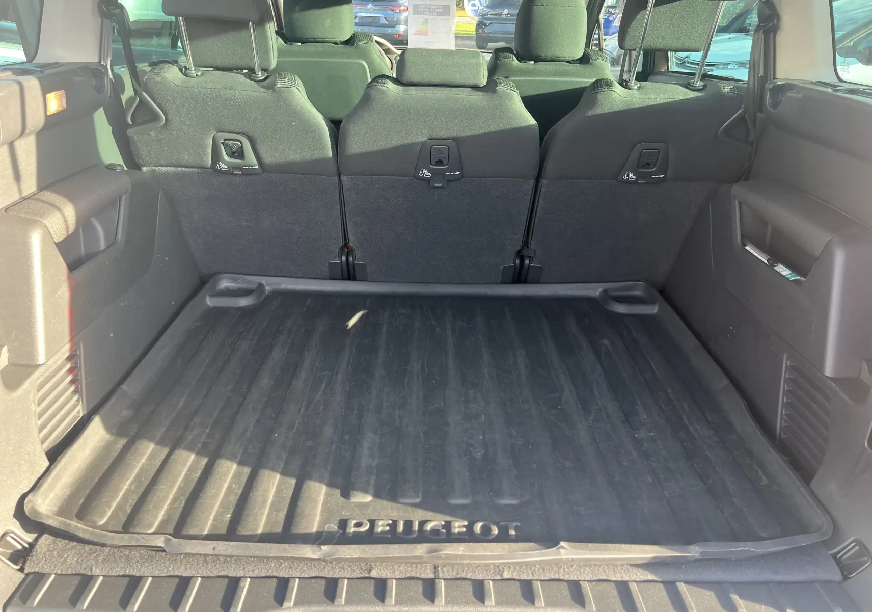 Coffre ouvert du Peugeot 5008 2013 montrant tapis de protection noir et sièges arrière rabattables en tissu noir.