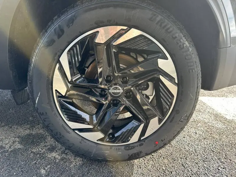 Gros plan sur la jante noire et argentée du Nissan Qashqai Hybrid e-POWER 2025 en Gris Argile, roue côté gauche.