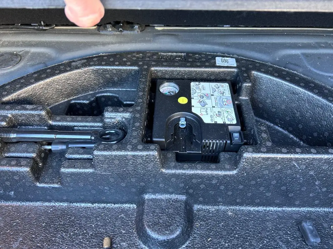 Vue rapprochée du compartiment à outils dans le coffre d'une KIA CEE'D gris 2022, montrant un compresseur et une clé.