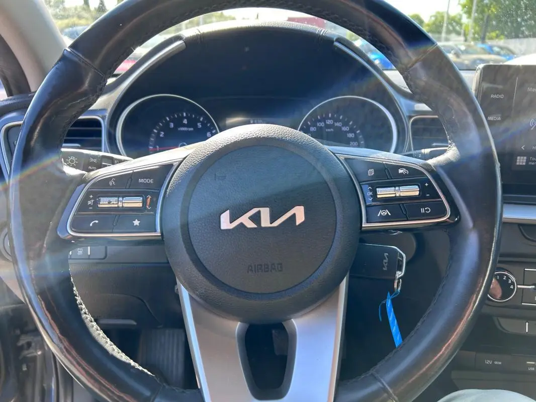 Vue rapprochée du volant noir de la Kia CEE'D 2022 avec commandes intégrées et tableau de bord en arrière-plan.