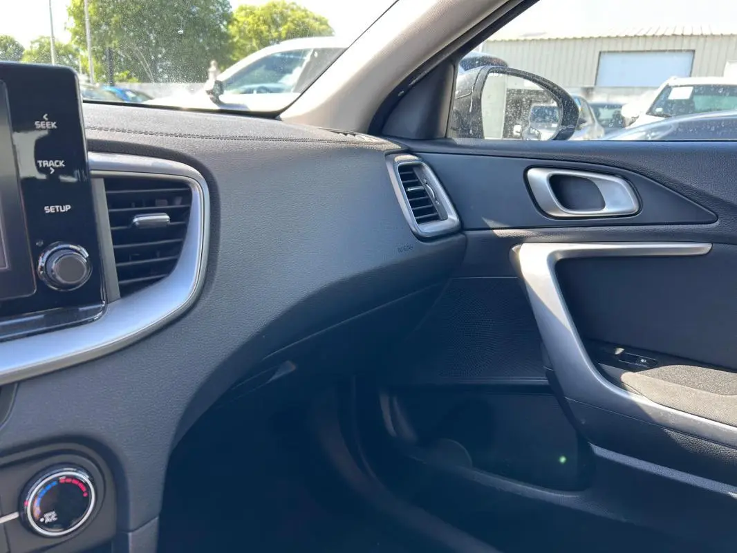 Intérieur côté passager de la Kia CEE'D gris 2022, montrant tableau de bord, aérateurs et porte avec poignée argentée.