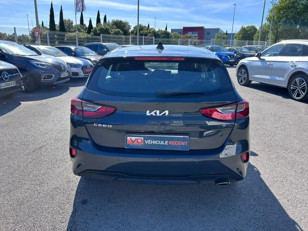 Vue arrière d'une KIA CEE'D gris 2022, avec feux arrière allumés et plaque "Véhicule récent" visible.