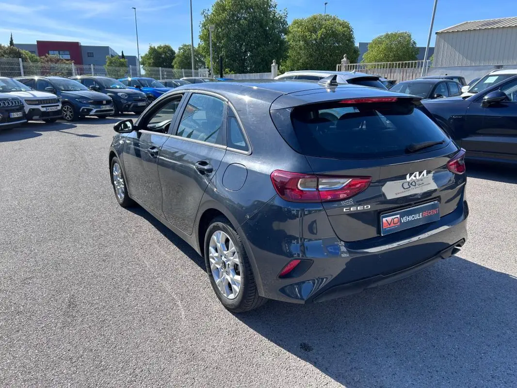 Vue 3/4 arrière droite d'une KIA CEE'D gris métallisé garée en extérieur sur un parking lumineux.