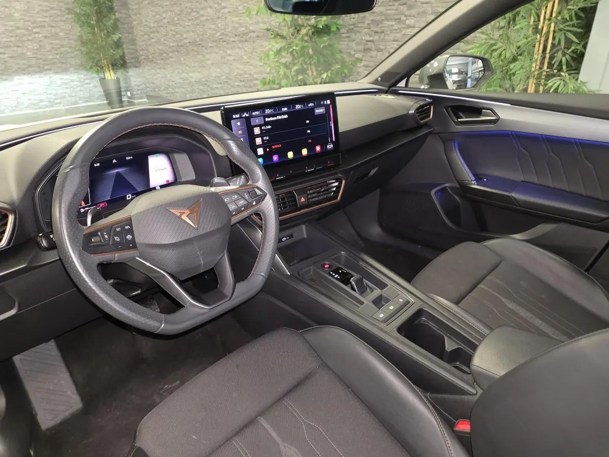 Vue intérieure côté conducteur de la CUPRA Leon 2023, volant cuir noir avec logo Copper et écran tactile central lumineux.