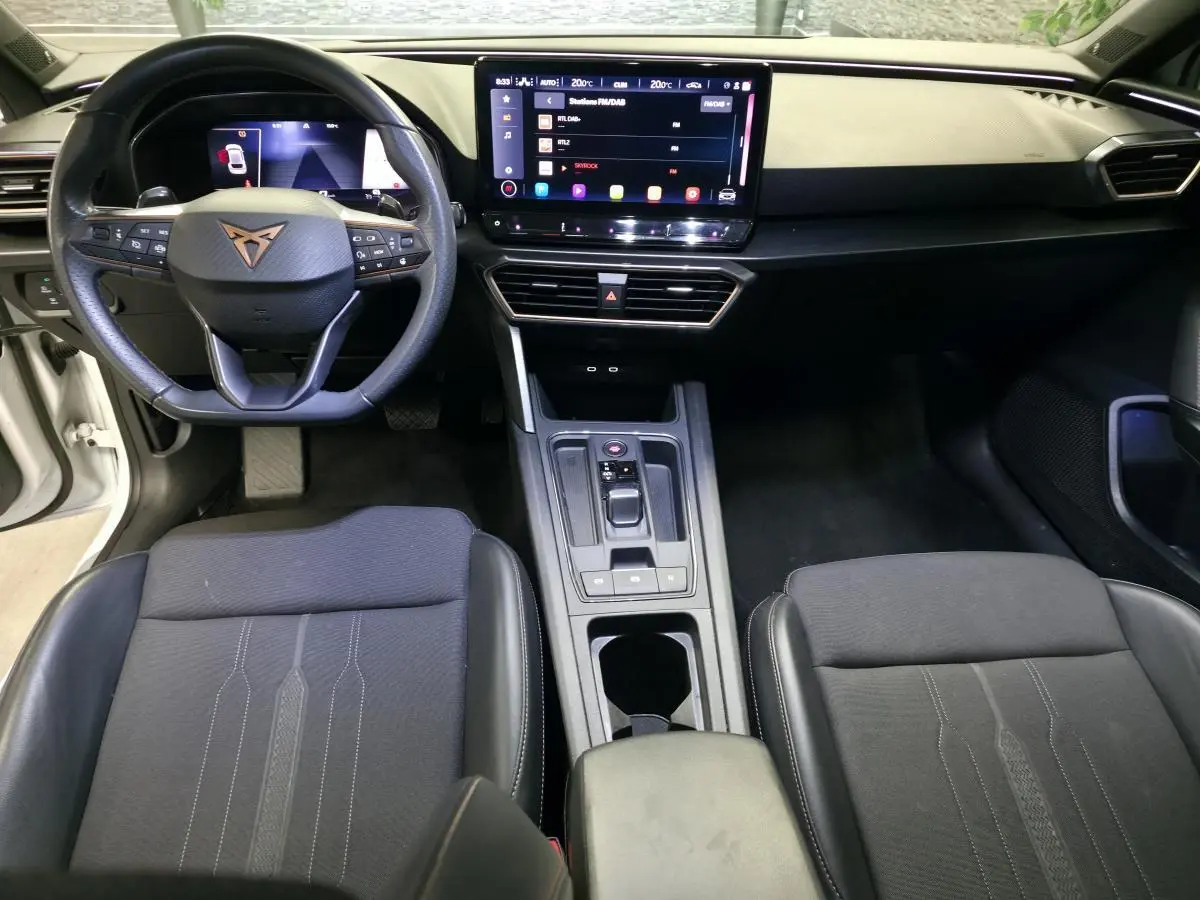 Vue intérieure avant de la CUPRA Leon 2023, volant cuir noir avec logo cuivre et écran tactile central HD.