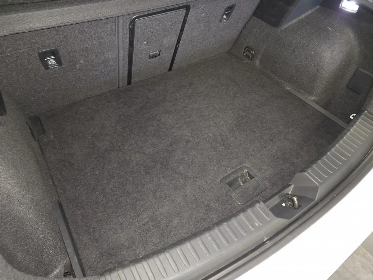 Coffre ouvert de la CUPRA Leon blanche, vue plongeante sur le tapis de coffre noir et les fixations internes.
