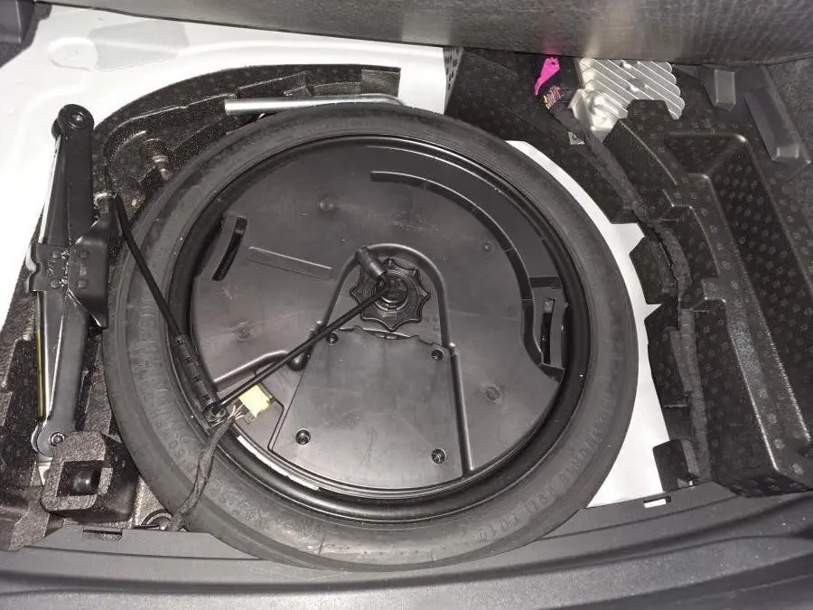 Vue rapprochée de la roue de secours et du cric dans le coffre d’une CUPRA Leon blanche 2023.