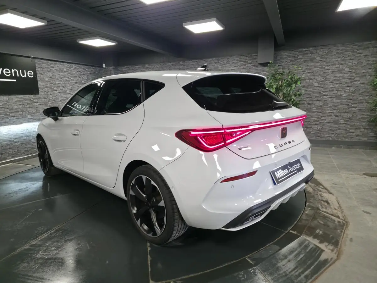 Vue 3/4 arrière droite d'une CUPRA Leon blanche avec feux arrière LED et jantes alliage noires en showroom.
