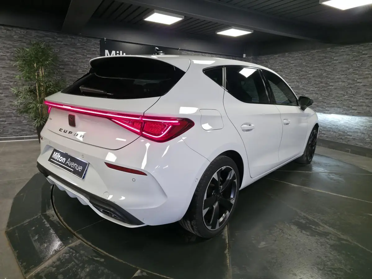 Vue 3/4 arrière droite d'une CUPRA Leon blanche Nevada avec feux arrière LED et jantes alliage noires.