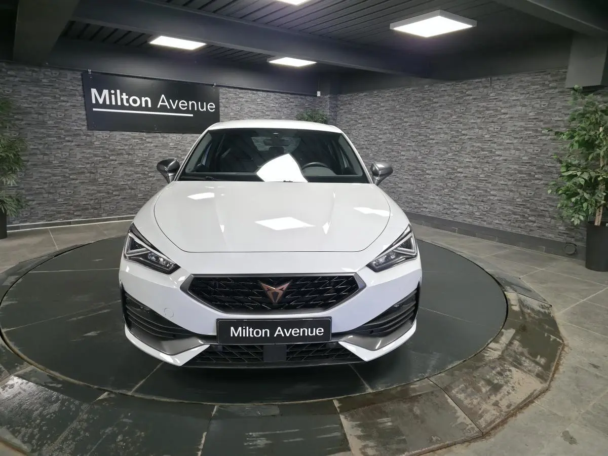Vue avant d'une CUPRA Leon blanche 2023 avec calandre noire et logo cuivre, sur plateau tournant en showroom.