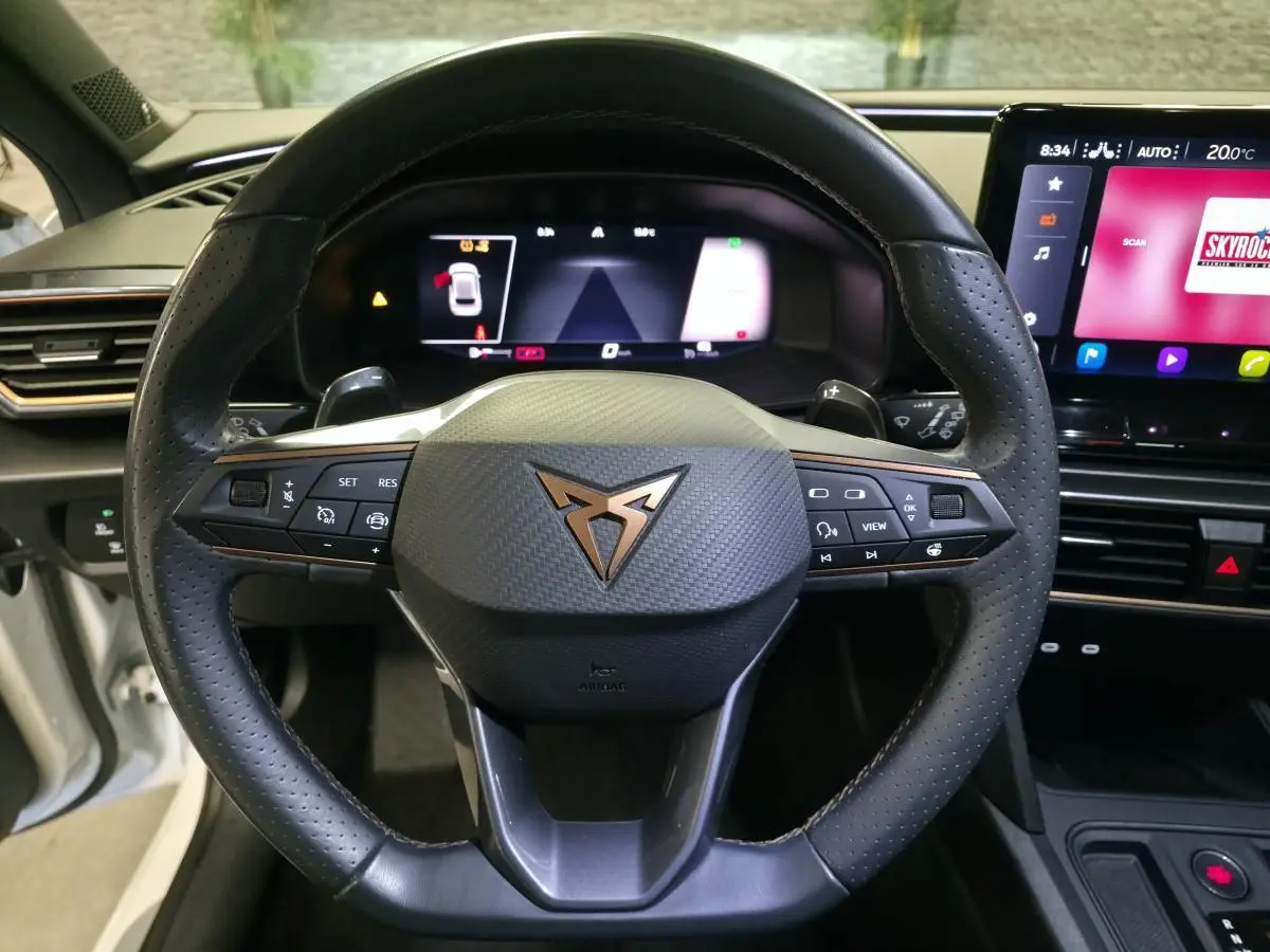Vue rapprochée du volant Cupra noir avec logo cuivre et tableau de bord digital du Leon 1.5e TSI blanc 2023.