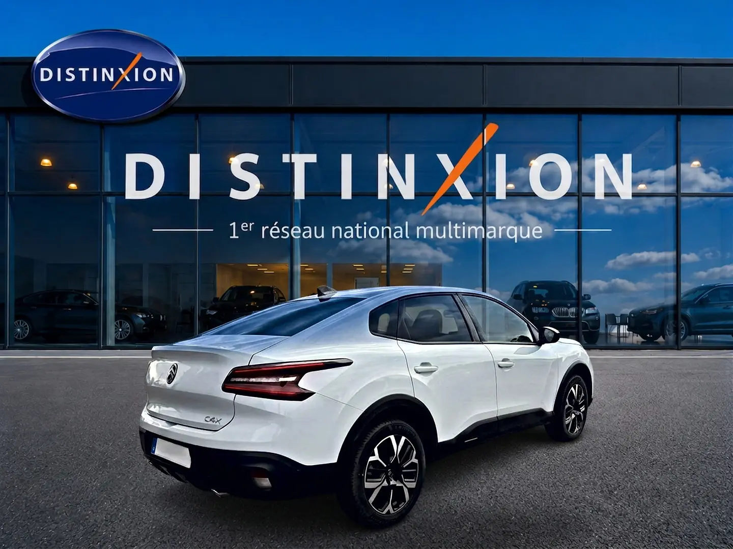 Vue 3/4 arrière droite d'une Citroën C4 X blanche avec feux arrière LED et jantes alu noires devant un showroom Distinxion.