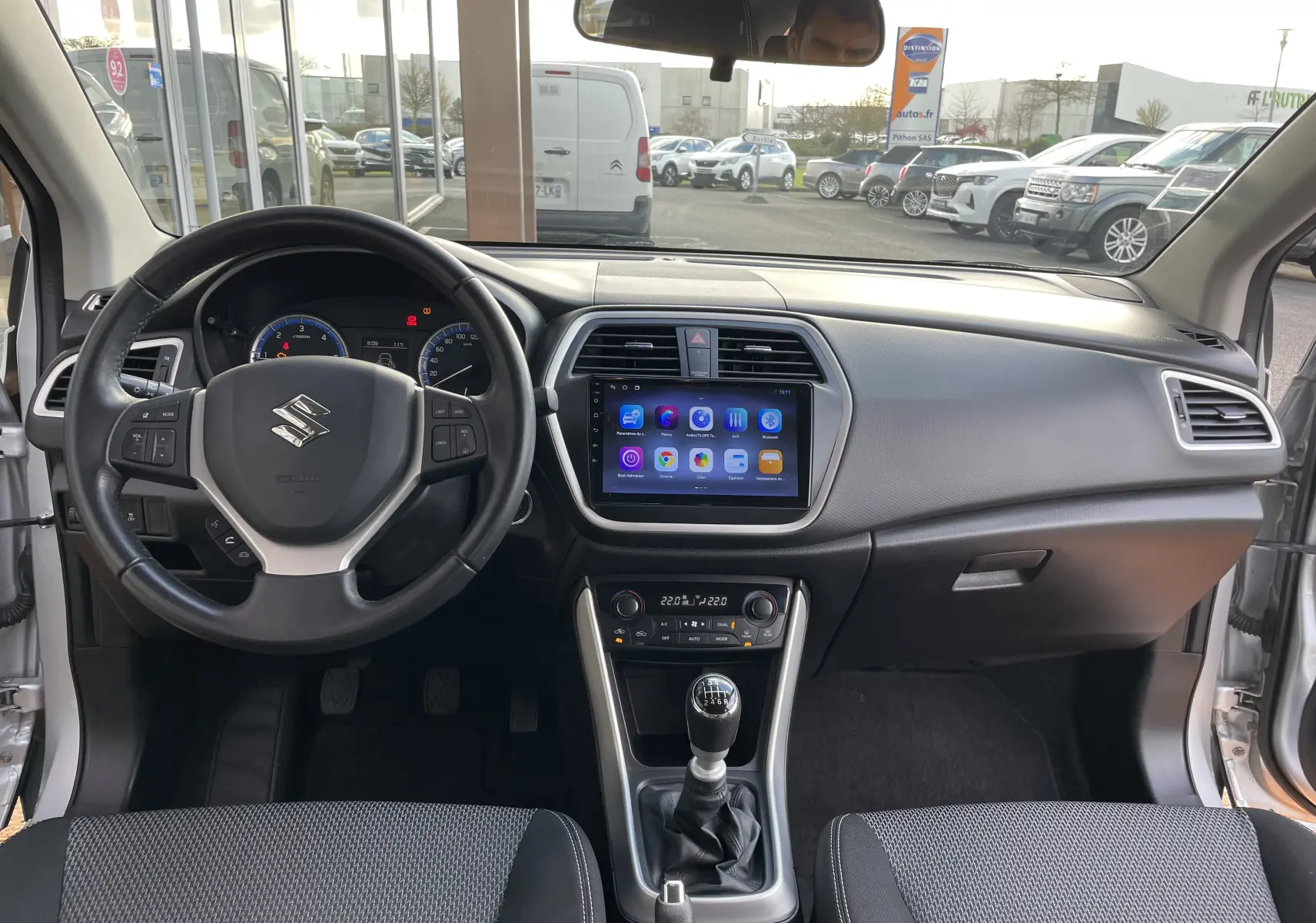 Vue intérieure avant du Suzuki SX4 S-Cross 2016 gris, avec tableau de bord moderne et écran tactile central.