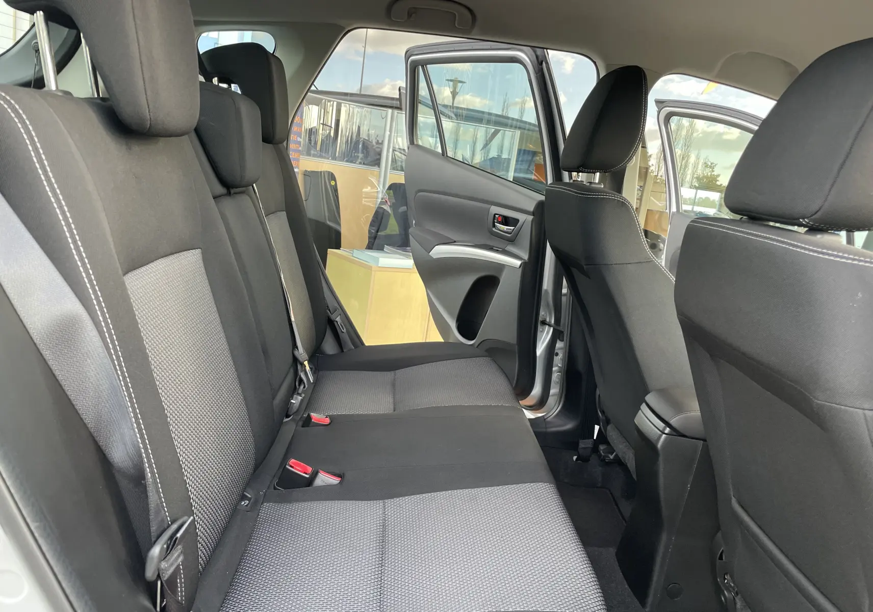 Vue intérieure côté gauche montrant la banquette arrière noire et grise du Suzuki SX4 S-Cross gris métallisé avec portes ouvertes.