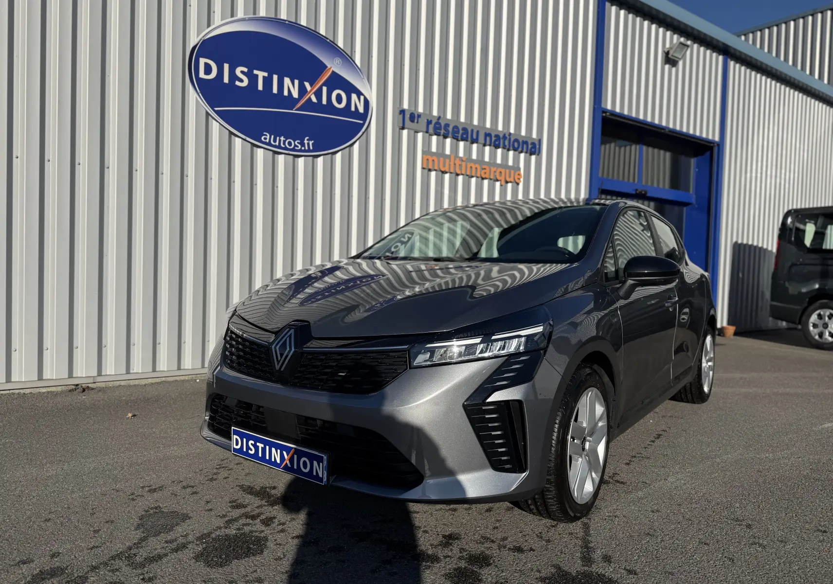 Renault Clio V gris schiste vue 3/4 avant droit, avec calandre noire et feux LED Pure Vision visibles.