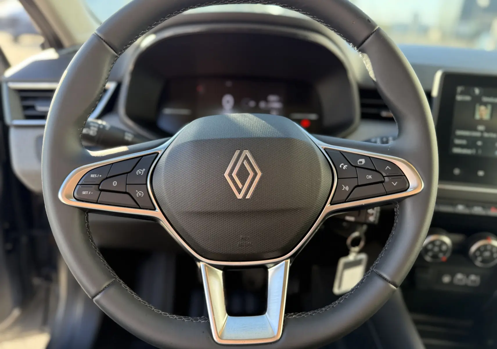 Gros plan sur le volant textile gainé de la Renault Clio V 1.5 dCi 100 gris schiste avec commandes intégrées.